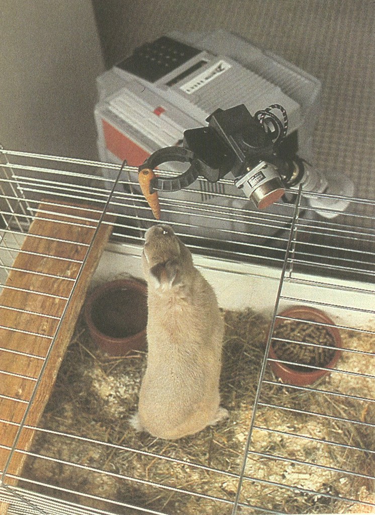Figure 2 — A HERO 1 using its optional five-axis arm and gripper to hold a carrot to a caged animal. Visible are the gripper closed on the carrot, the arm's wrist and forearm, and the keypad-and-di…